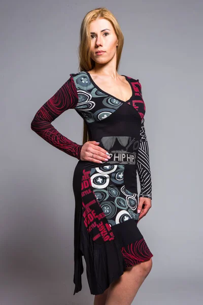 Young blonde in a dress with an abstract pattern on a gray background in the studio — Stock Photo, Image