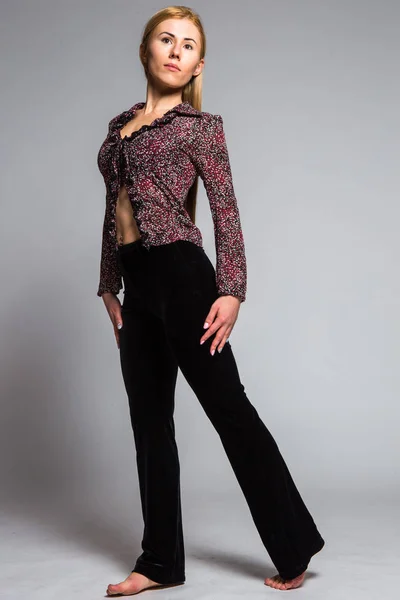 Young blonde in a translucent blouse and black pants on a gray background in the studio — Stock Photo, Image