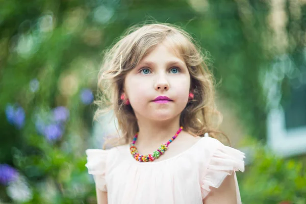 En tonårig flicka med ett halsband av pärlor runt halsen, en lila läppstift på läpparna mot en bakgrund av grönt bladverk — Stockfoto