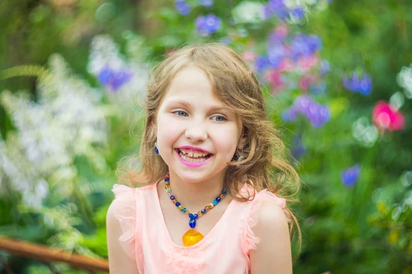 A teenage girl with a necklace of beads around her neck, a purple lipstick on her lips against a background of green foliage — Stock Photo, Image