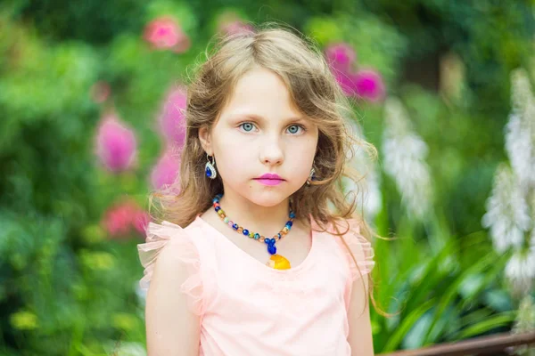 Una ragazza adolescente con una collana di perline intorno al collo, un rossetto viola sulle labbra su uno sfondo di fogliame verde — Foto Stock