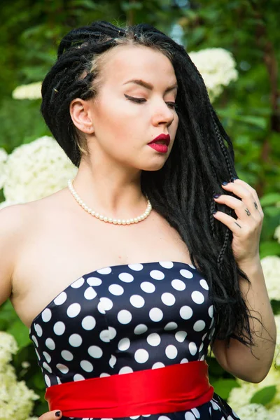Young girl in vintage black dress in white peas with black dreadlocks on head and red lipstick on lips — Stock Photo, Image