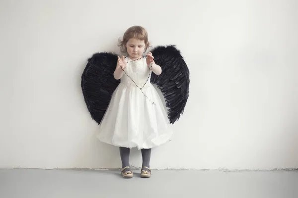 Menina em vestido branco com asas pretas artificiais — Fotografia de Stock