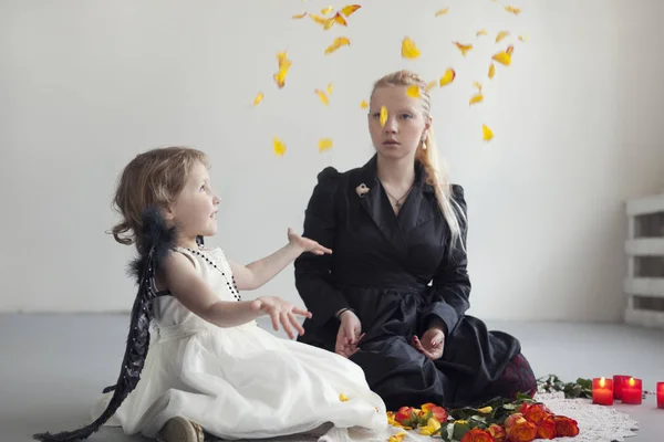 Kleines Mädchen im weißen Kleid mit künstlichen schwarzen Flügeln sitzt mit Mama auf dem Boden — Stockfoto