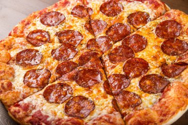 Tahta bir tabakta pizza sosisi, salam ve peynir dilimlerine ayrılmış.