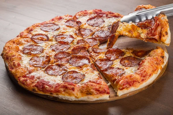 Cut into pieces of pizza sausage, salami and cheese on a wooden platter — Stock Photo, Image