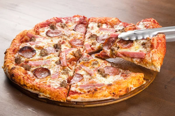 Нарізати шматочки піци ковбасою, салямі та сиром на дерев'яній тарілці — стокове фото