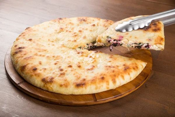 Snij in stukken pizza met vlees, olijven en champignons op een houten schotel — Stockfoto