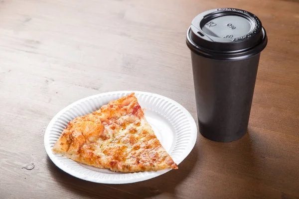 Um pedaço de pizza em uma caixa de papelão individual e uma xícara de plástico para café — Fotografia de Stock