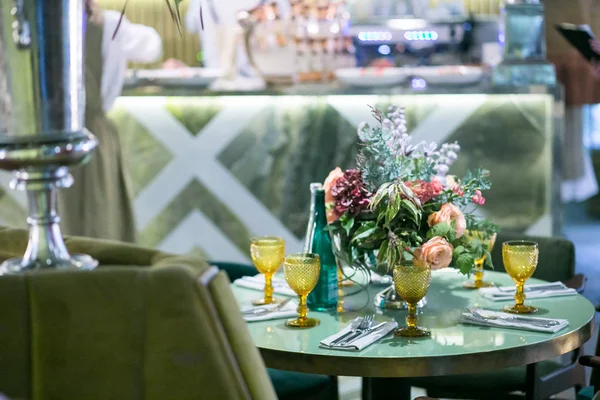Стол на обед: столовые приборы, стаканы из желтого стекла и букет цветов в металлической вазе на ноге — стоковое фото