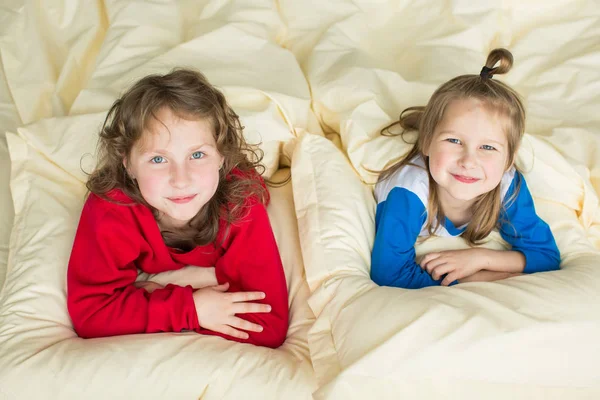 Gargalhada de pijama vermelho e um menino de pijama azul jazem na cama — Fotografia de Stock