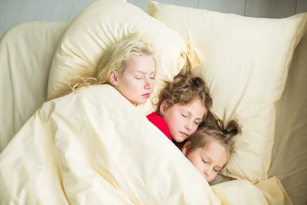 Een familie ligt onder een deken in bed — Stockfoto