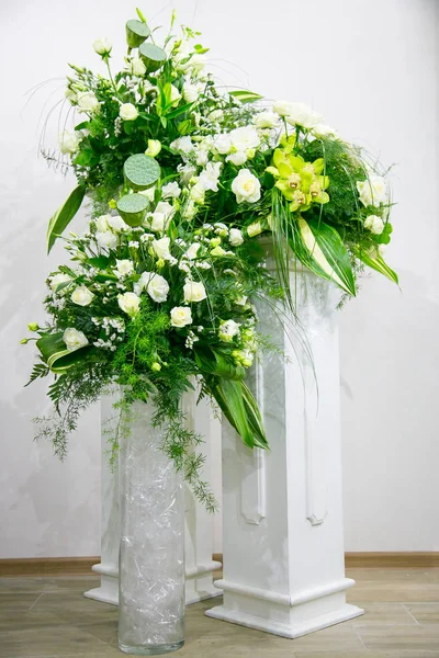 En bukett med vita rosor, gula påskliljor, grönska och lotusblommor står i en vas på en marmor stå — Stockfoto