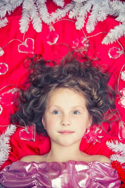 彼女の頭の周りクリスマスのガーランドとモミの枝と赤い床の上に横たわる小さな金髪の女の子 — ストック写真