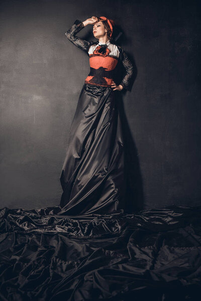 Young beautiful dark-haired woman in a felt hat, long black skirt and red corset