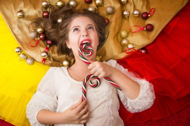 Beyaz, zarif elbiseli, elinde şekerle altın bir arka planda uzanan bir kız.