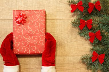 Yeni yıl / yılbaşı hediye paketi, eller kırmızı eldiven ve ağaç ahşap arka plan şablonu üzerinde kırmızı yay ile