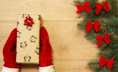 Yeni yıl / yılbaşı hediye paketi, eller kırmızı eldiven ve ağaç ahşap arka plan şablonu üzerinde kırmızı yay ile