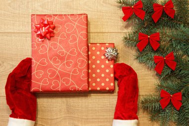 Yeni yıl / yılbaşı hediye paketi, eller kırmızı eldiven ve ağaç ahşap arka plan şablonu üzerinde kırmızı yay ile