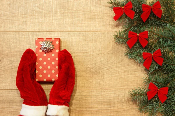 Yeni yıl / yılbaşı hediye paketi, eller kırmızı eldiven ve ağaç ahşap arka plan şablonu üzerinde kırmızı yay ile