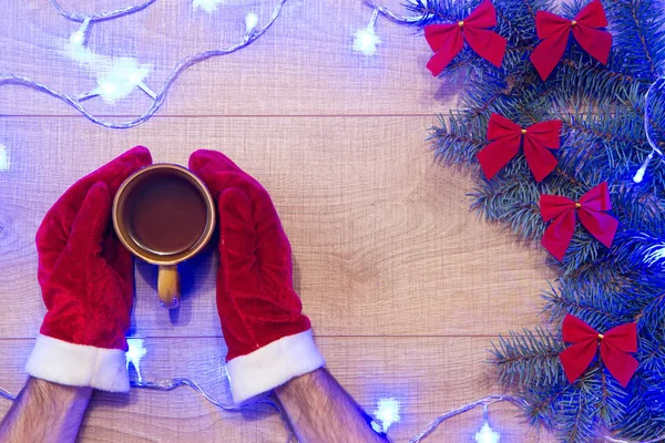 圣诞树用红色的蝴蝶结 蓝色的花环和手在红色的手套与杯红茶在木制背景模板 — 图库照片