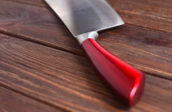 Beautiful knife with a red handle on a wooden table.