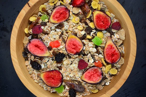 Healthy organic fitness food in a natural wooden plate. Muesli with fruits on a stone background.