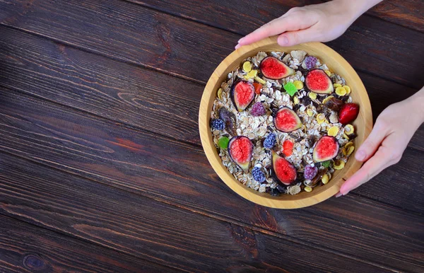 Top view concept of a healthy fitness breakfast. Woman holds a wooden plate with muesli and fruits. Organic natural food on a textured wooden table.