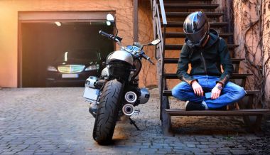 Yalnız motorcu hakkında düşünce ve motosiklet yakınındaki merdivenlerde dinlenmiş. Motosiklet ve motosikletçi bir şehir sokak üzerinde bir kask içinde. 