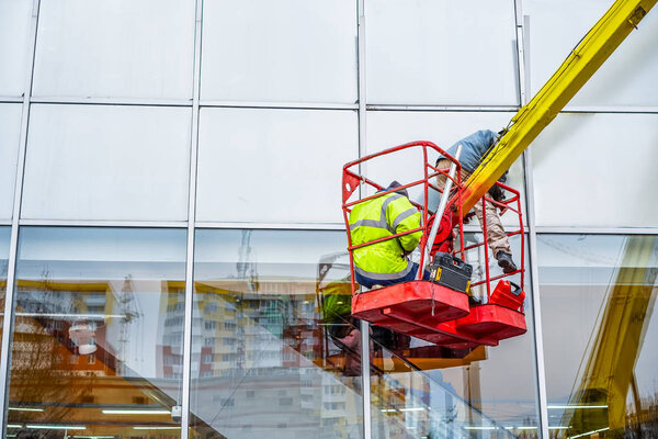 High-altitude installation works.  Professional installation work on a telescopic boom lift platform. Workers fix the window in building.