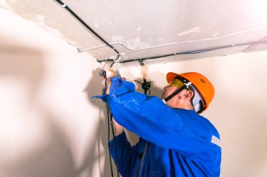 Sert şapkalı ve üniformalı elektrikçi çekiç matkabıyla çalışır.