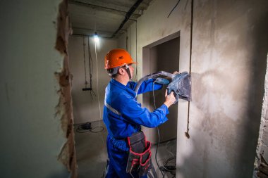 Duvar oluğu kesme makinesi. Elektrikçi, profesyonel ekipmanlarla duvarda oyuk açıyor. Elektrik takibi kesiliyor. Kapalı alan inşaatı ve onarım geçmişi. 