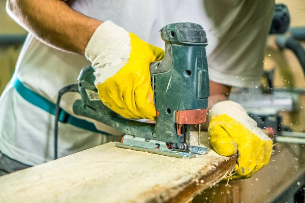 Carpenter hands with fretsaw. Carpenter use electric fretsaw to cut the desk. Carpentry workshop background.