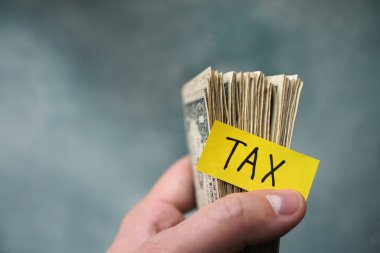 Taxes concept with one dollar bills in a hand and text Tax.