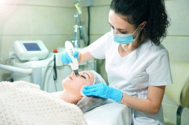 Kozmetik uzmanı genç kadın için ultrasonik yüz bakımı yapıyor. Soyuluyor.