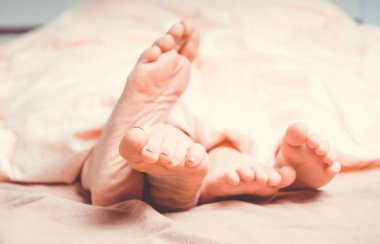 Anne ve bebek ayakları battaniyenin altından dışarı bakıyor. Rahat yatakta sıcak bir sabah.. 
