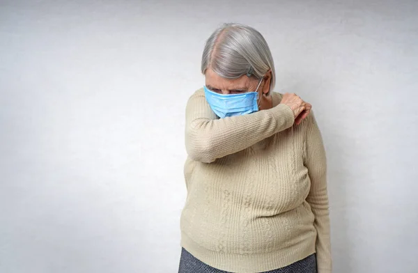 How to cough right concept. An elderly woman in a medical mask coughs while hiding with her hand