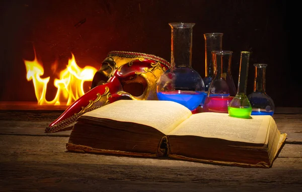 Medieval alchemy and pharmacy concept with old book, traditional mask and bottles with medicine.