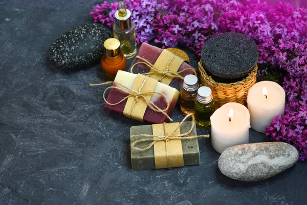 SPA still life with handmade soap, aroma candles, lilac flowers, aromatic oils and stones on the dark background — Stock Photo, Image