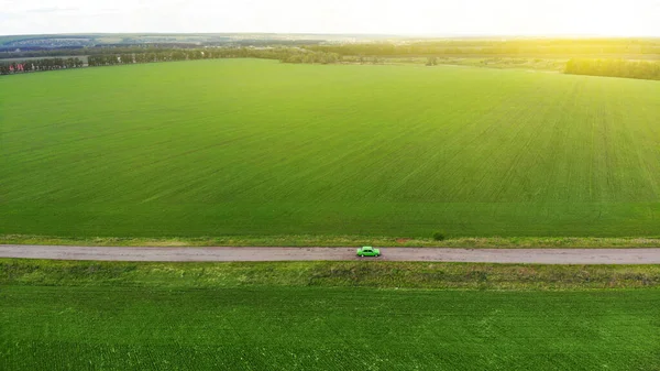 Aereo. Auto verde divertente guida lungo la strada asfaltata rustica tra i campi. Vista sopra dal drone — Foto Stock