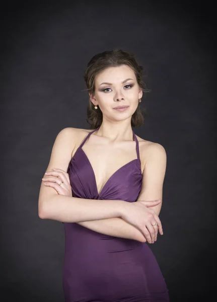 Una chica joven y sonriente en vestido posando sobre un fondo oscuro . — Foto de Stock