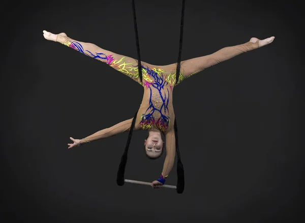A young girl performs the acrobatic elements in the air trapeze. Studio shooting performances on a black background.