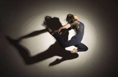 Karanlıkta kız jimnastik atlama gerçekleştirir, beyaz bir arka plan üzerinde bir şekil bir gölge var.