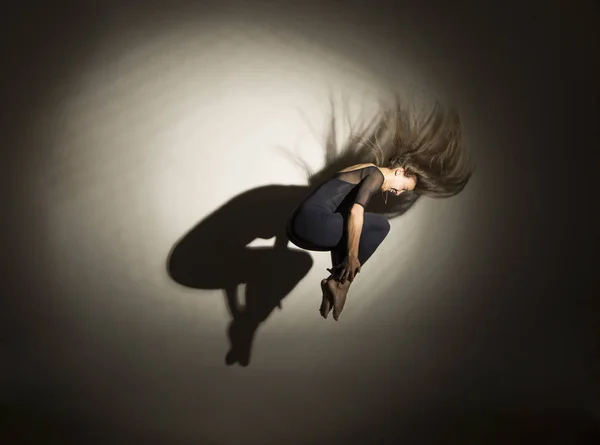 暗闇の中の女の子は体操ジャンプを行い、白い背景には形から影があります. — ストック写真
