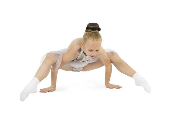 A little girl in a light stage costume performs gymnastic exercises on a white background. — Stock Photo, Image