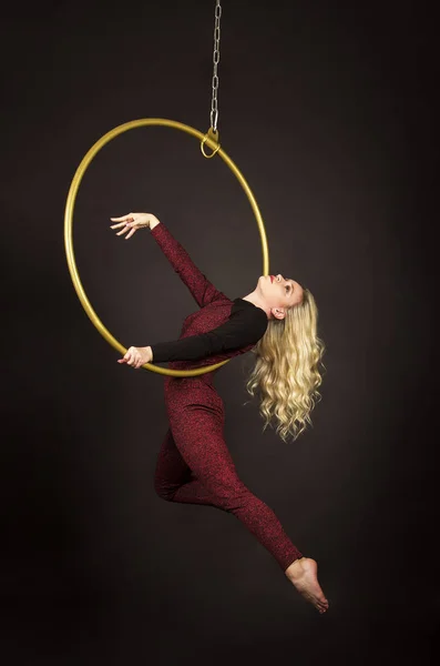 A slender blonde girl-an air acrobat in a red suit with long hair , performs exercises in an air ring.