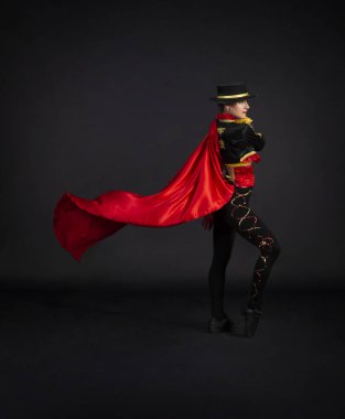 Boğa güreşçisi olarak stilize edilmiş bir sahne kostümüyle zarif bir şekilde dans eden plastik kız. Karanlık bir arkaplanda stüdyo çekimi.