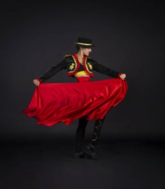 Boğa güreşçisi olarak stilize edilmiş bir sahne kostümüyle zarif bir şekilde dans eden plastik kız. Karanlık bir arkaplanda stüdyo çekimi.