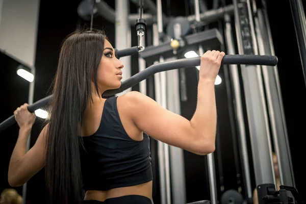 Deporte, fitness, trabajo en equipo y concepto de personas - mujer joven flexionando los músculos en la máquina de gimnasio y entrenador personal con portapapeles — Foto de Stock