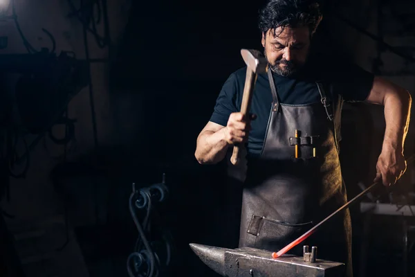 Ferreiro sênior forjando o metal fundido na bigorna em ferreiro . — Fotografia de Stock